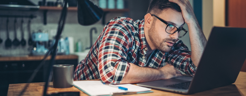 man slumped over at computer looking somewhat stressed