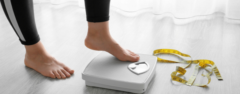 person stepping on scale with measuring tape by their feet