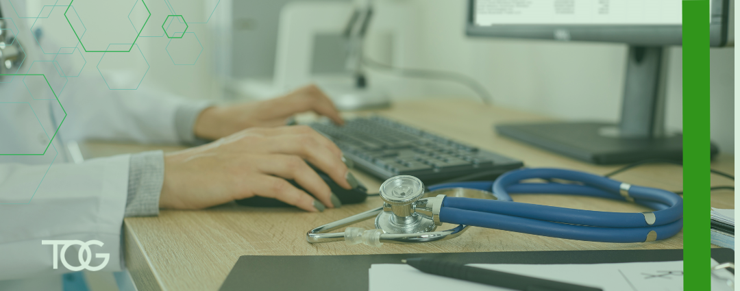 A female doctor in a white lab coat with painted finger nails fingernails types on a computer with a stethoscope in the foreground.