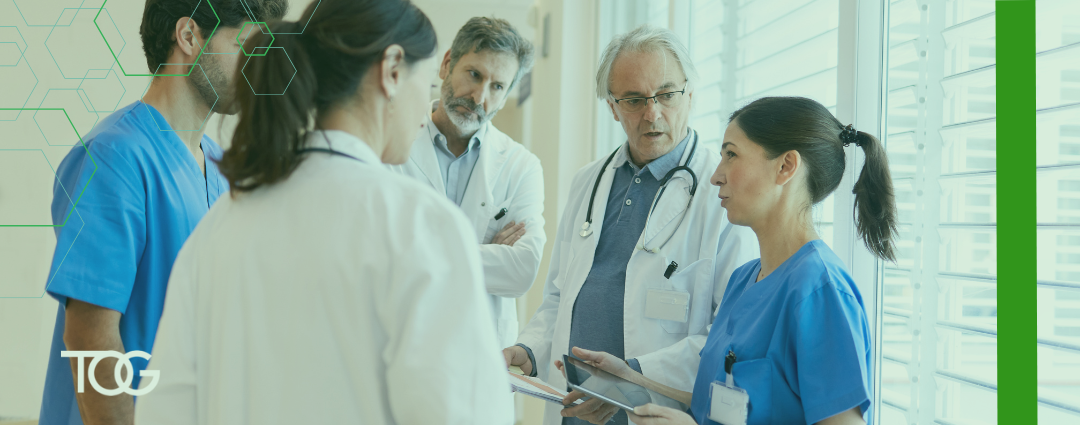 Five health care workers meeting in a hospital hallway with serious expressions on their faces.