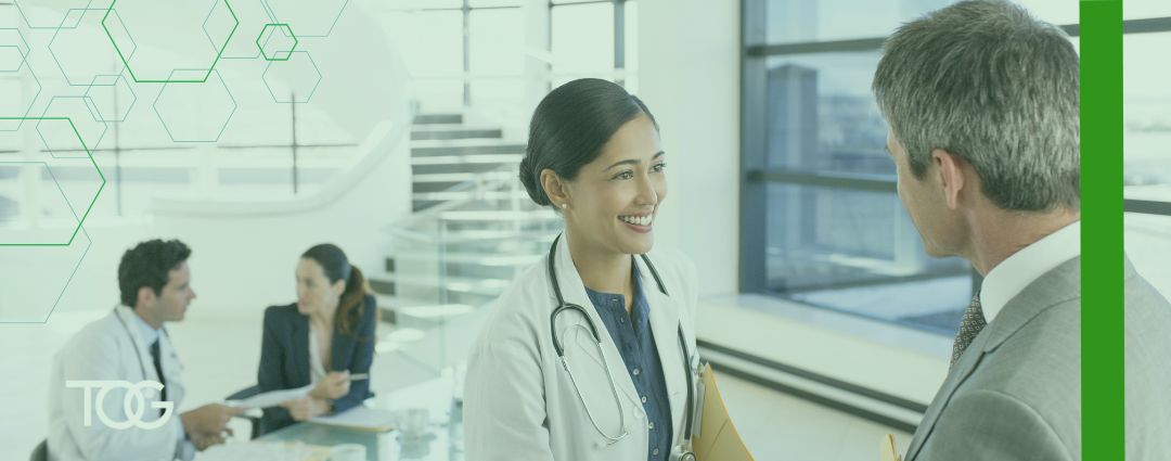 Doctor greeting business professional with a man and a woman having a meeting in the background.