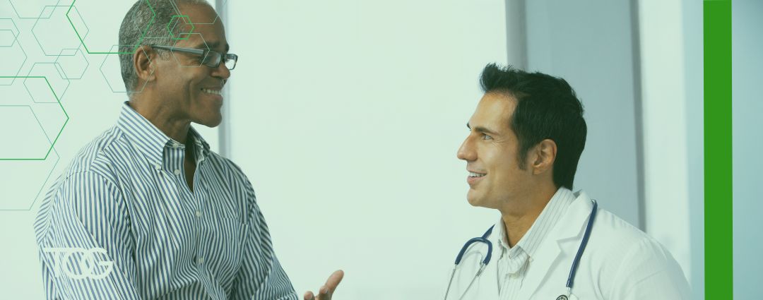 Doctor on left meets with smiling male patient who is wearing black-rimmed glasses.