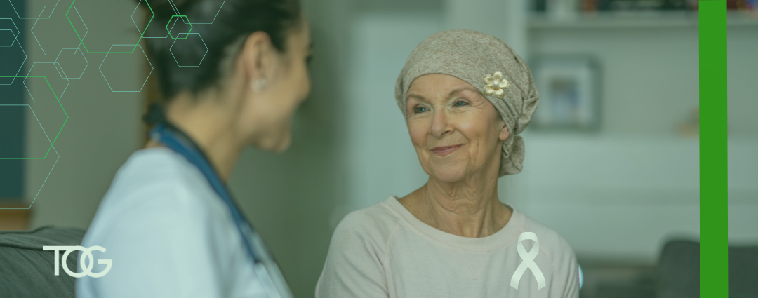 An older woman wearing a beige headscarf smiles while speaking with a healthcare professional wearing a stethoscope. A white cancer awareness ribbon appears in the lower right, with green geometric graphics and branding elements framing the image.