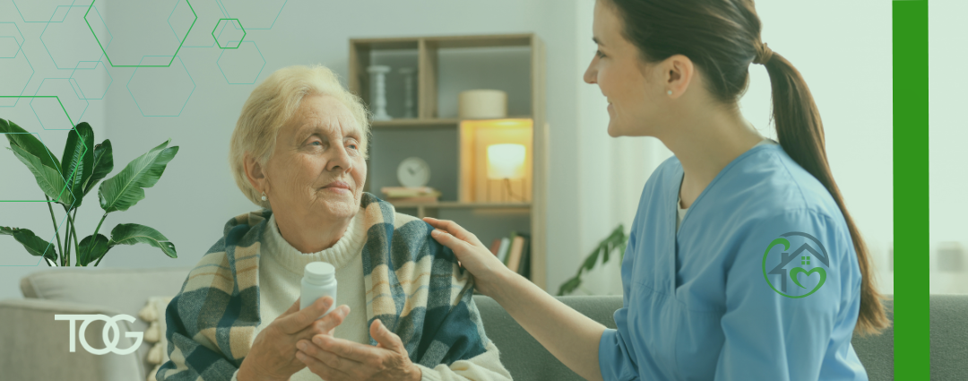 Elder female patient wearing a plaid shawl and a cream turtleneck holds a white prescription bottle while receiving a comforting hand on her left shoulder from a young female health care worker wearing blue scrubs.